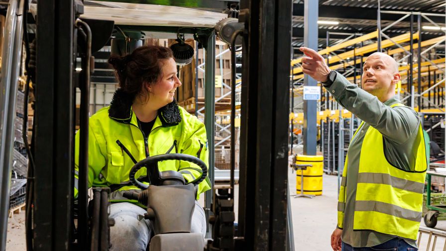 Vrouw in heftuck kijkt naar rechts naar collega die wijst
