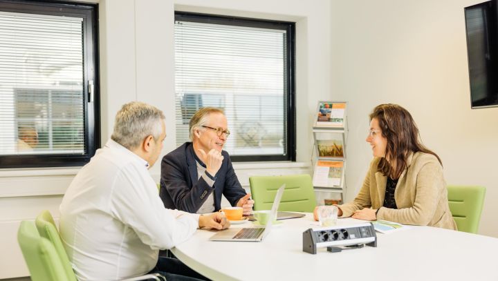 Drie mensen aan een tafel in gesprek met elkaar